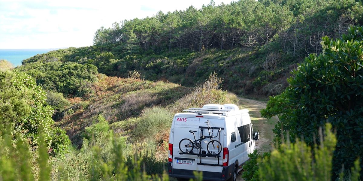 a van parked on a dirt road with a bike mounted to the back of it