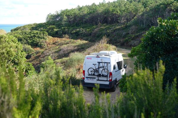 a van parked on a dirt road with a bike mounted to the back of it