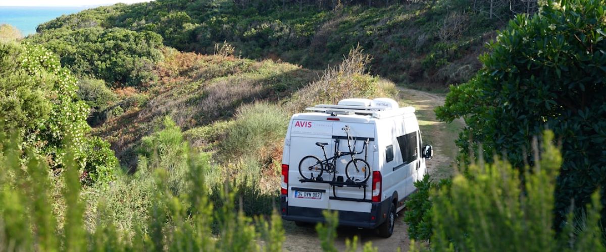 a van parked on a dirt road with a bike mounted to the back of it