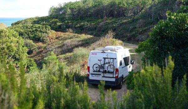 a van parked on a dirt road with a bike mounted to the back of it